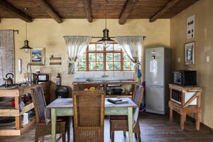 A rustic kitchen with wooden furniture, a refrigerator, a microwave, and a window with curtains.