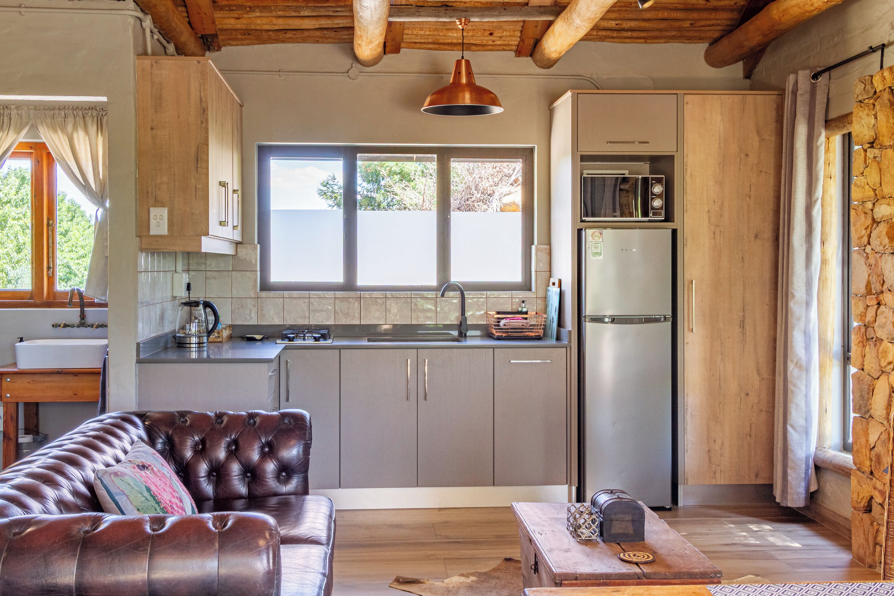 A compact kitchen with a modern refrigerator, a microwave, and a sink. There is a leather sofa and a wooden coffee table in the living area.