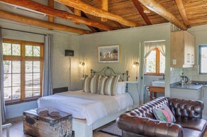 A bedroom with a bed, a wooden bench, a leather sofa, a small table, and a window with curtains.