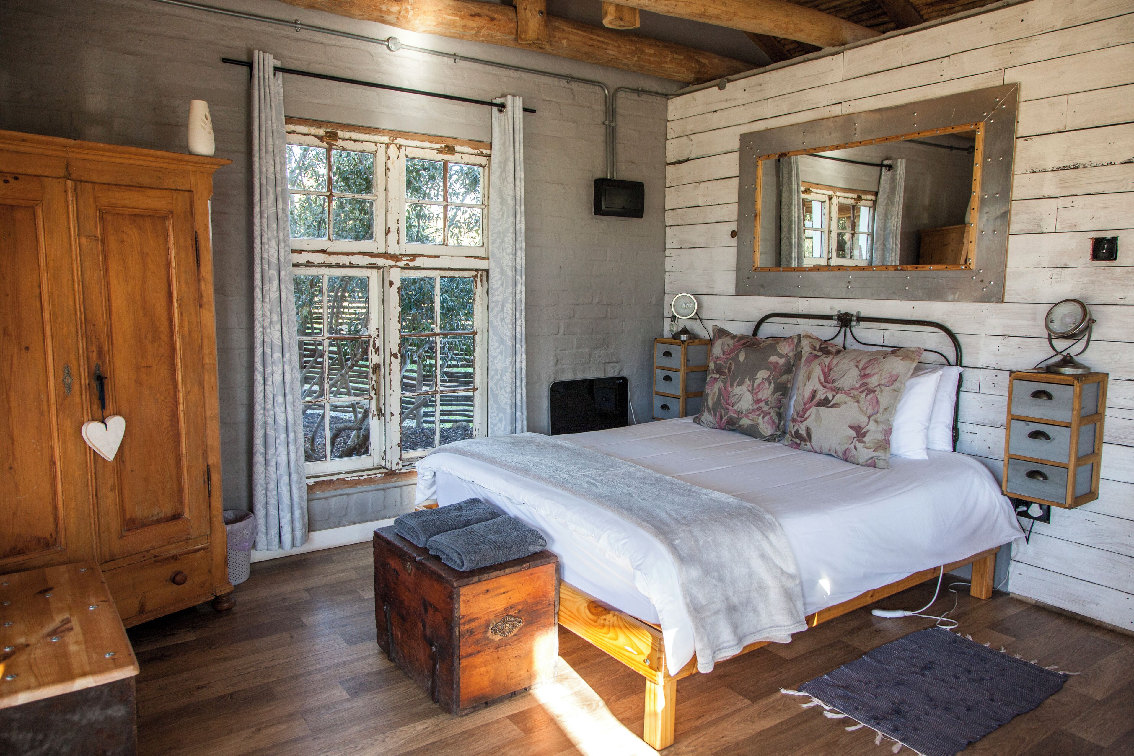 Un dormitorio con una cama de madera, un aparador, un cómoda, un espejo y una ventana con cortinas.