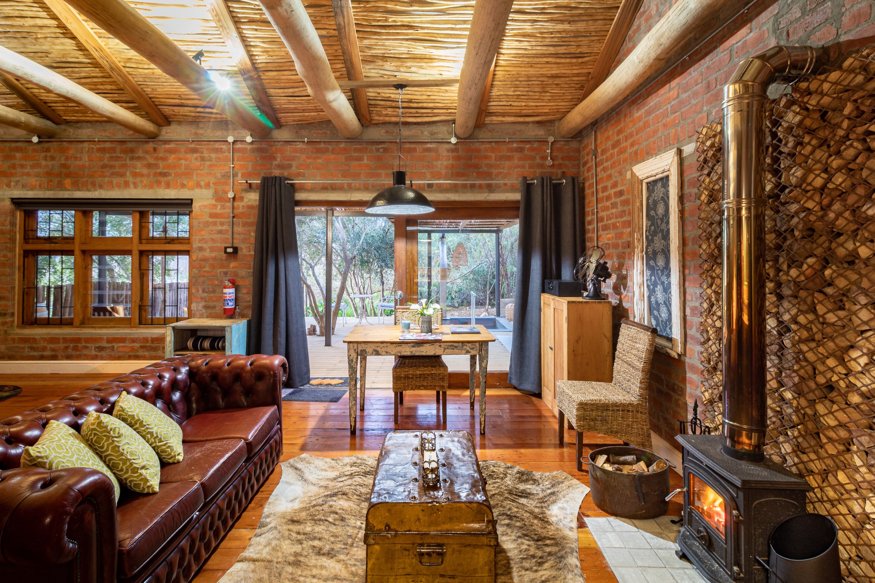 Un interior rústico con un sofá de cuero, una mesa de madera, una chimenea y vistas amplias a través de grandes ventanales.