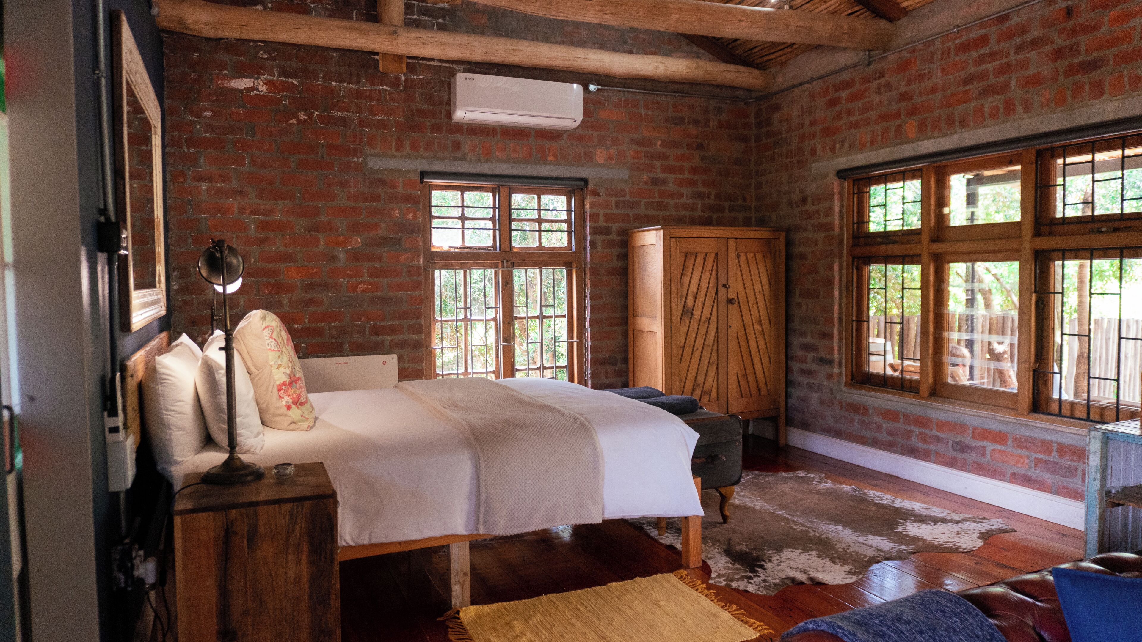 A rustic room with a bed, wooden furniture, and large windows.