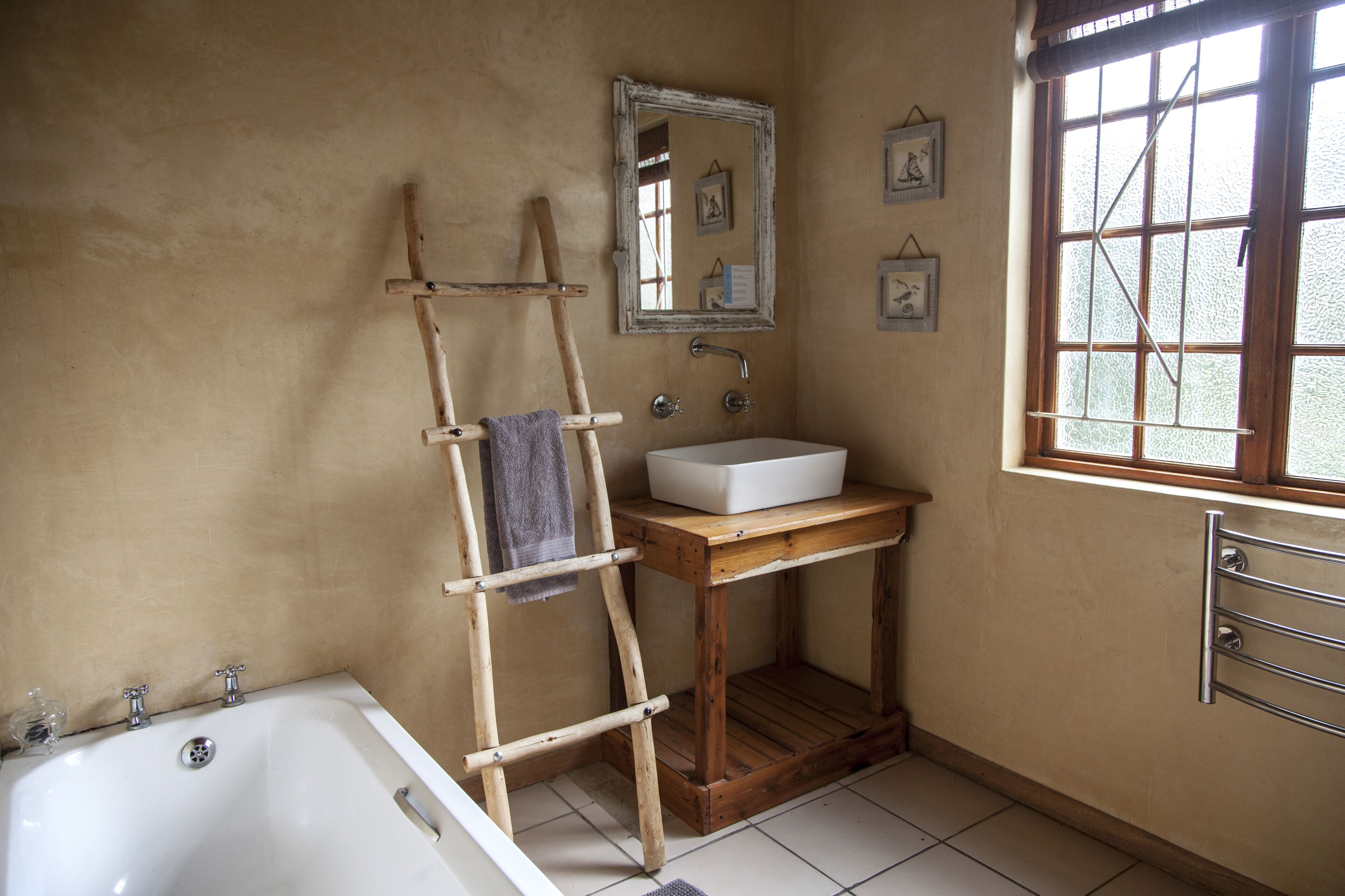 Un baño con una escalera de madera, un lavamanos blanco y un ventanal grande.