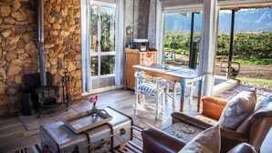 A rustic interior with stone walls, a wooden table, and a view of a vineyard. - Bergsicht Country Farm Cottages (Tulbagh)