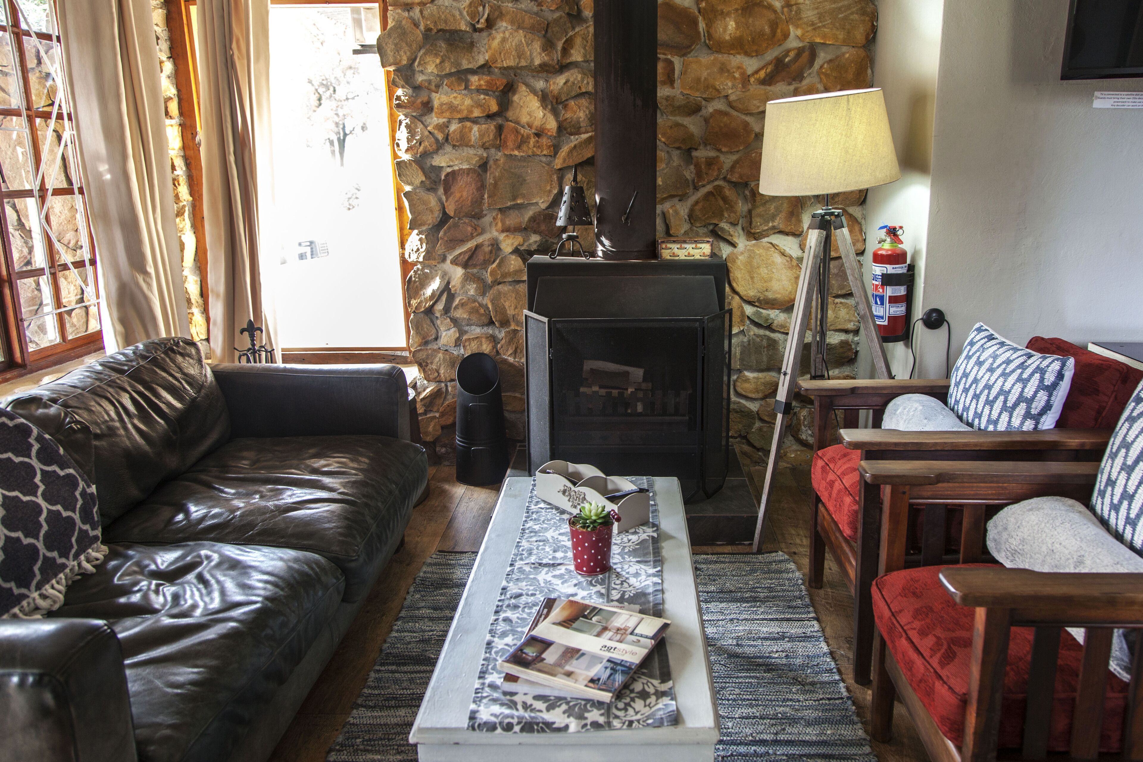 A cozy living room with a stone wall, leather sofa, wooden chairs, a fireplace, and a coffee table with magazines.