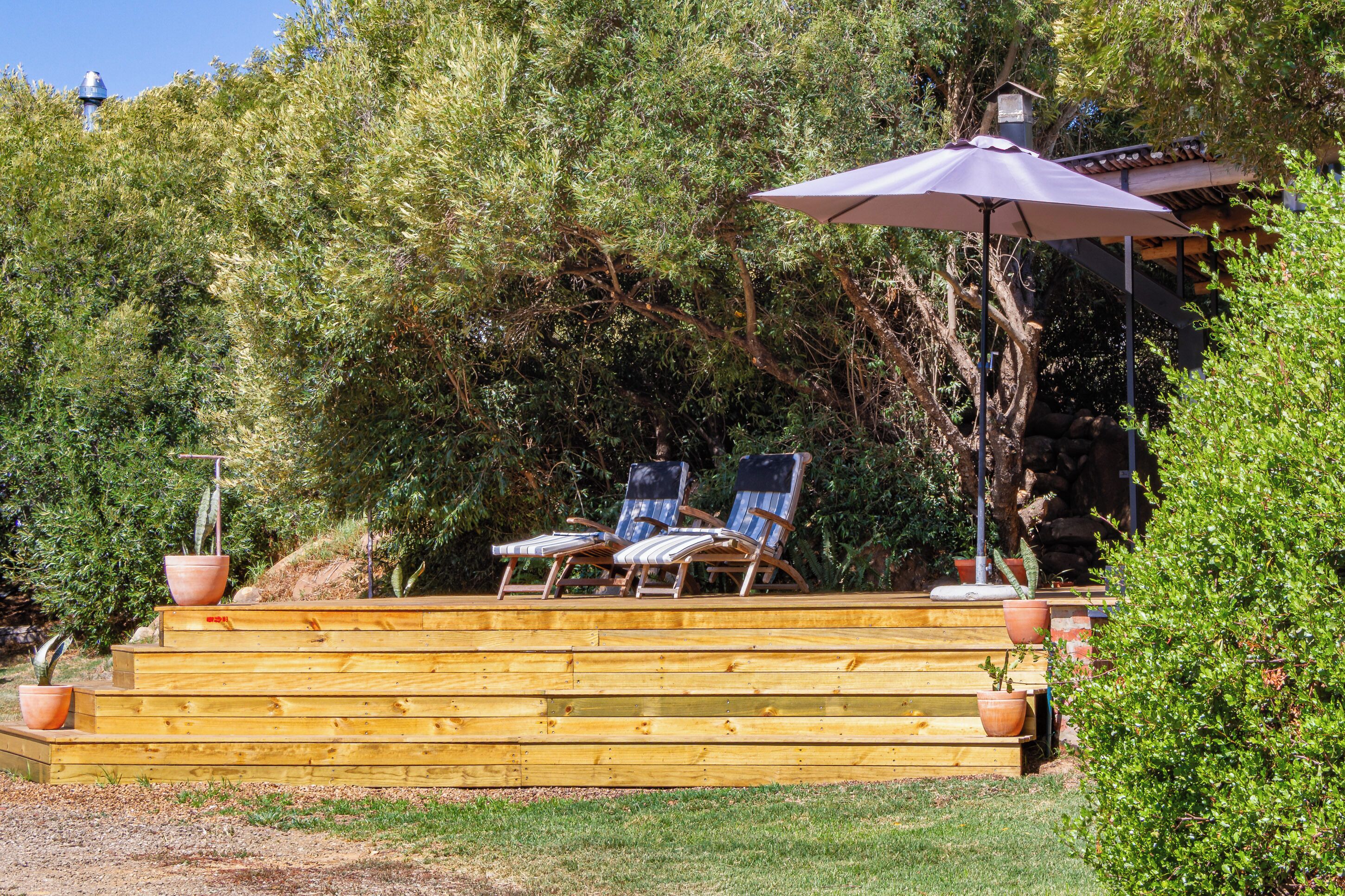 Eine Holzterrasse mit Stufen zu einem Sitzbereich, der zwei Liegestühle und einen großen Sonnenschirm umfasst.