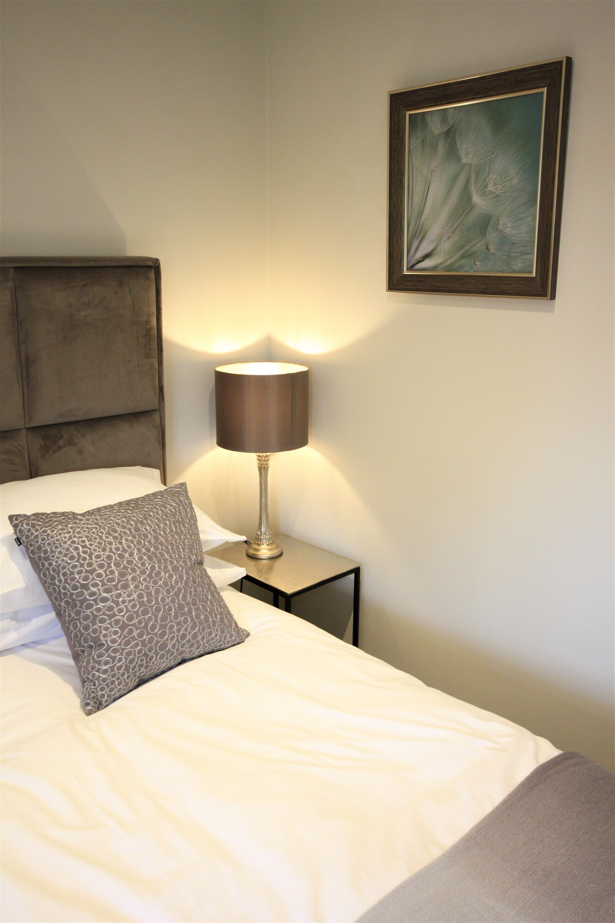 A neatly made bed with a patterned pillow, a bedside lamp, and a framed artwork on the wall.