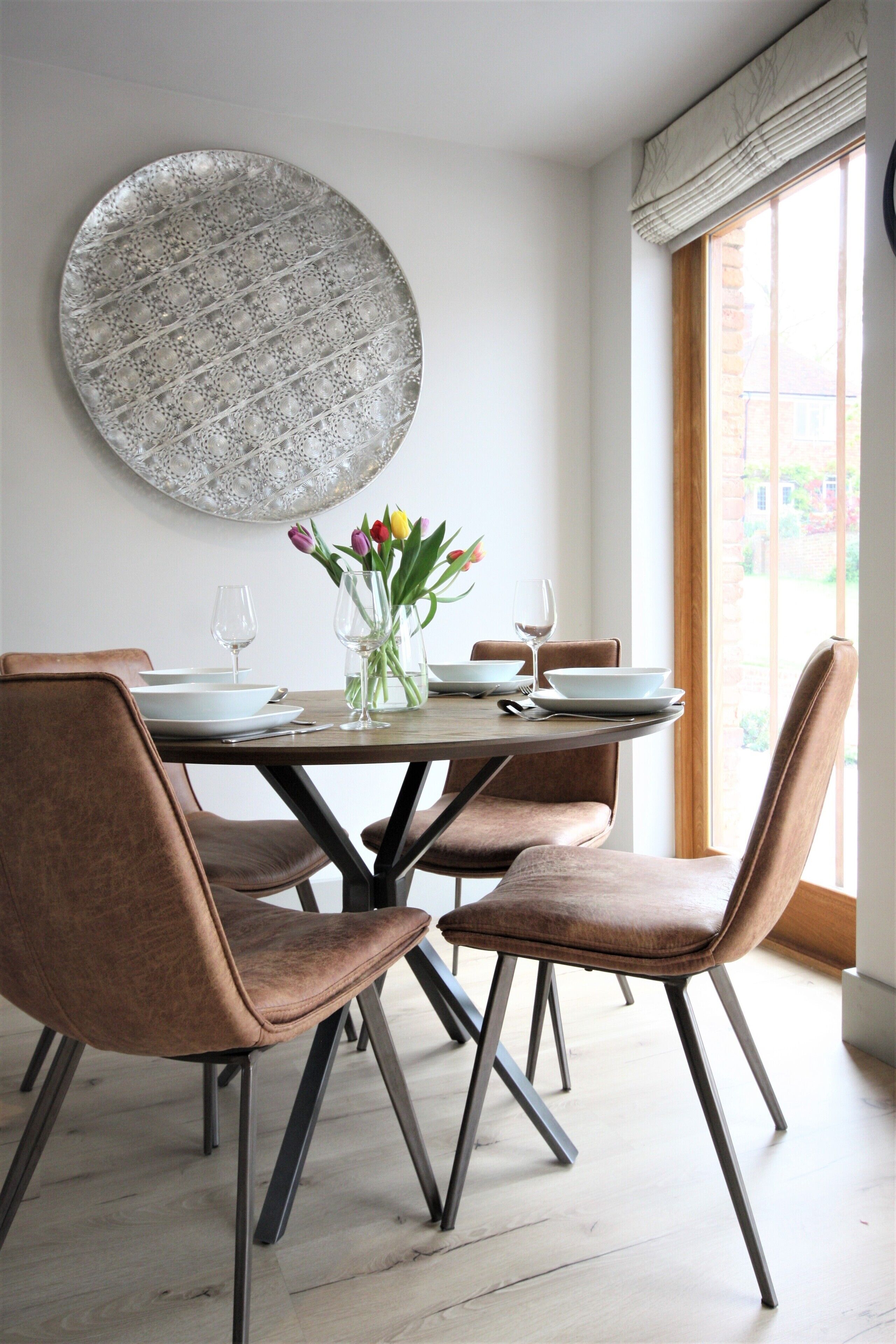 Un coin repas avec une table ronde, quatre chaises et un vase rempli de fleurs.