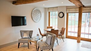 A modern living room with a glass coffee table, patterned armchairs, a flat-screen TV, and a large window with a view of the outdoors. - 3 Weaver's Cottage - ideal retreat for exploring (Benenden)