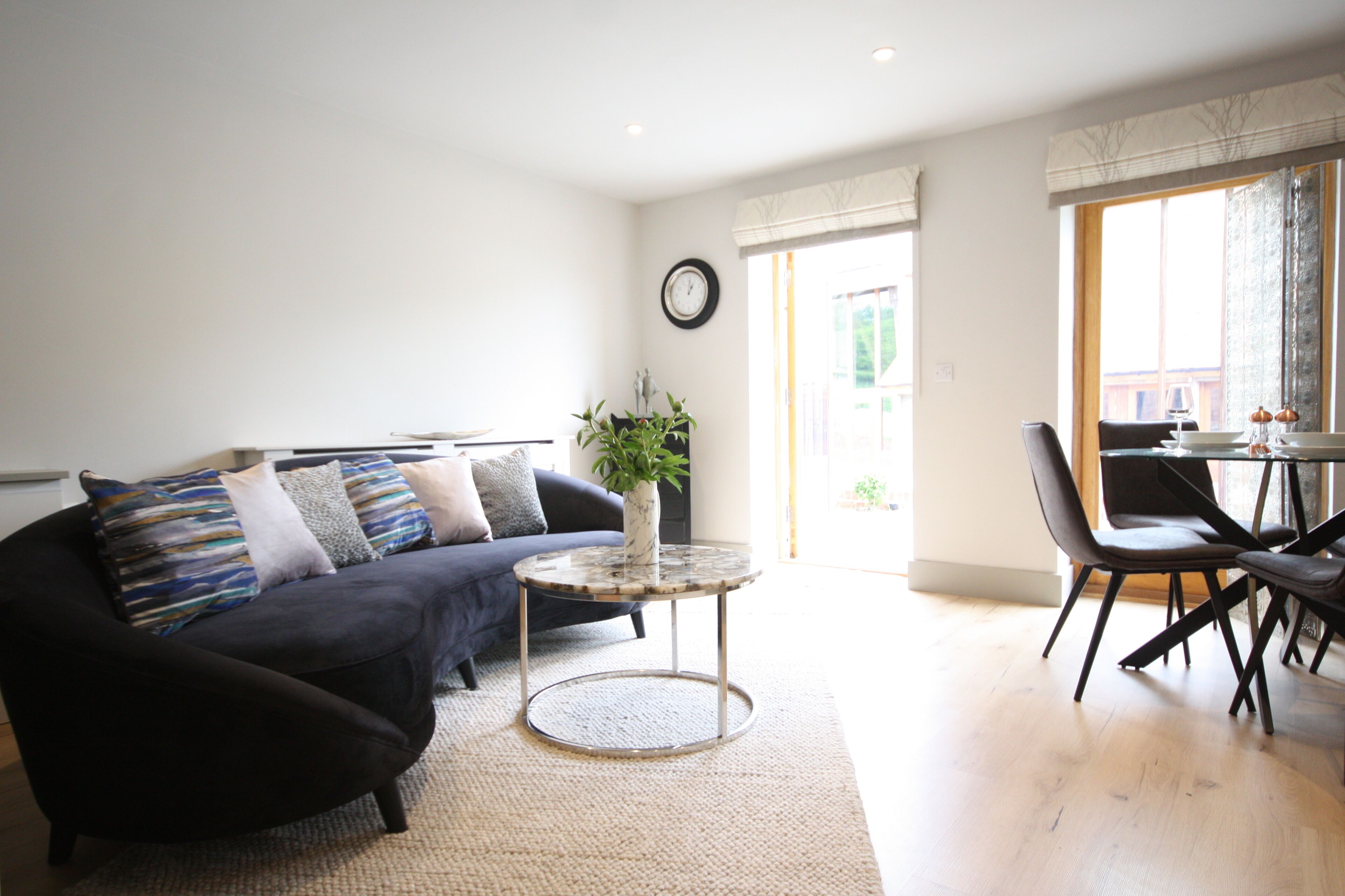 Ein modernes Wohnzimmer mit einem dunklen Sofa, einem runden Couchtisch und einem Essbereich mit Stühlen und einem Tisch.