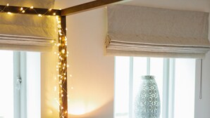 Une chambre à coucher avec un lit, une lampe, un vase sur le rebord de la fenêtre et des guirlandes lumineuses.