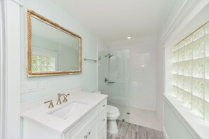 A bathroom with a white vanity, a large mirror, a shower, and a toilet. - Beach Breeze (Anna Maria)