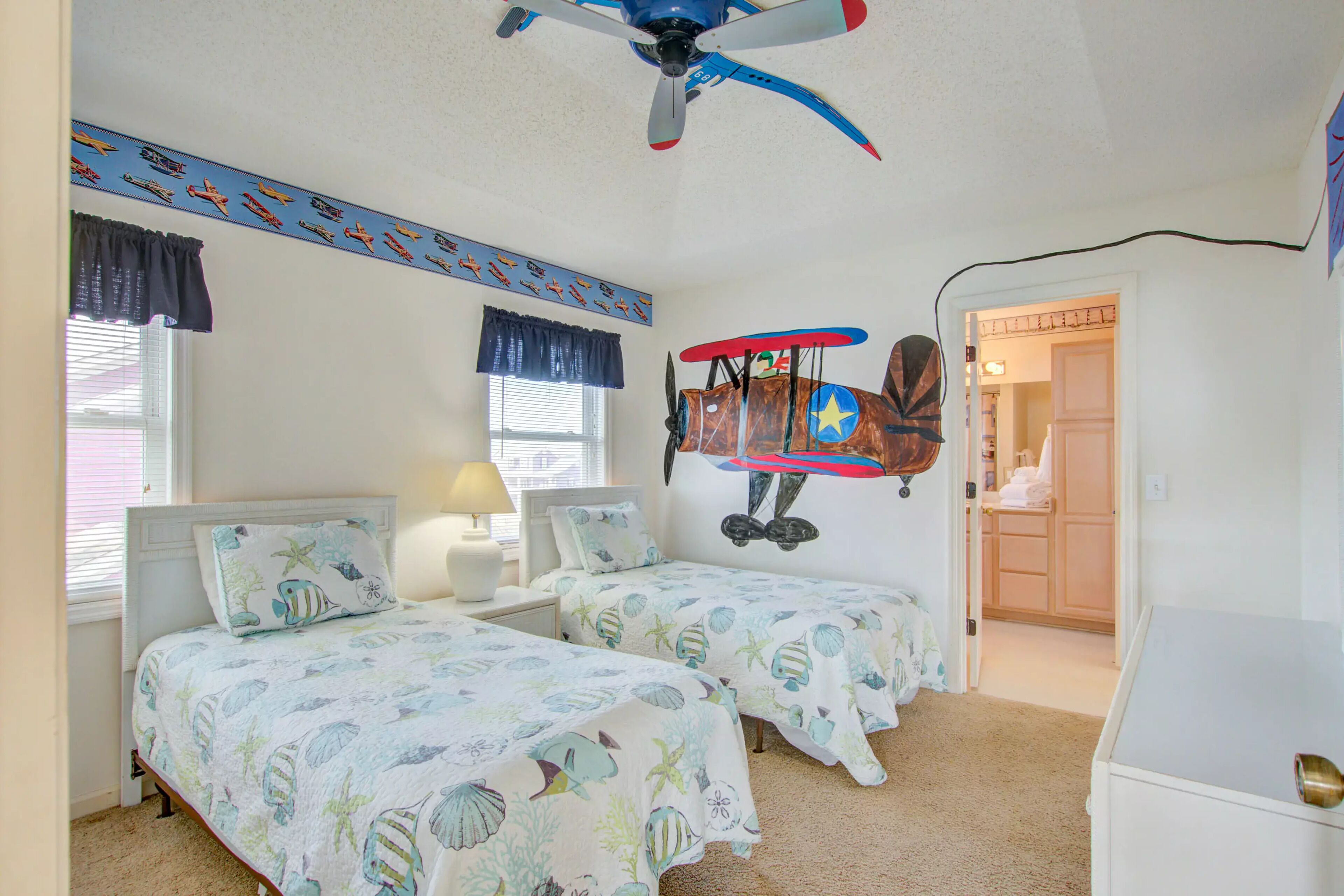 A bedroom with two beds, a ceiling fan, and a wall-mounted airplane decoration.