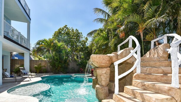 A swimming pool with a stone waterfall, a white staircase, and lounge chairs. - Ocean Breeze (Bradenton Beach)