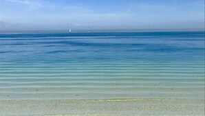 A beach with clear water and a distant sailboat. - Ocean Breeze (Bradenton Beach)
