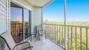 Ein Balkon mit zwei Stühlen und einem kleinen Tisch, mit Blick auf eine Landschaft mit Bäumen und einem Gebäude in der Ferne.