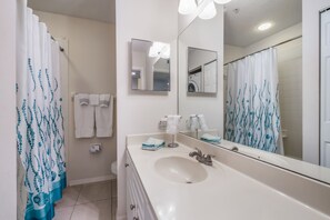 Un baño con lavamanos blanco, un espejo y una cortina de ducha con estampado azul.