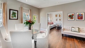 A spacious living room with a dining area, featuring a white sofa, a glass-top dining table, and a large window with curtains. - You will Love this Charming Townhouse in West Palm Beach, West Palm Beach Villa 1862 (West Palm Beach)