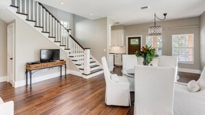 A modern living room with a wooden floor, white furniture, a staircase, and a kitchen area. - You will Love this Charming Townhouse in West Palm Beach, West Palm Beach Villa 1862 (West Palm Beach)