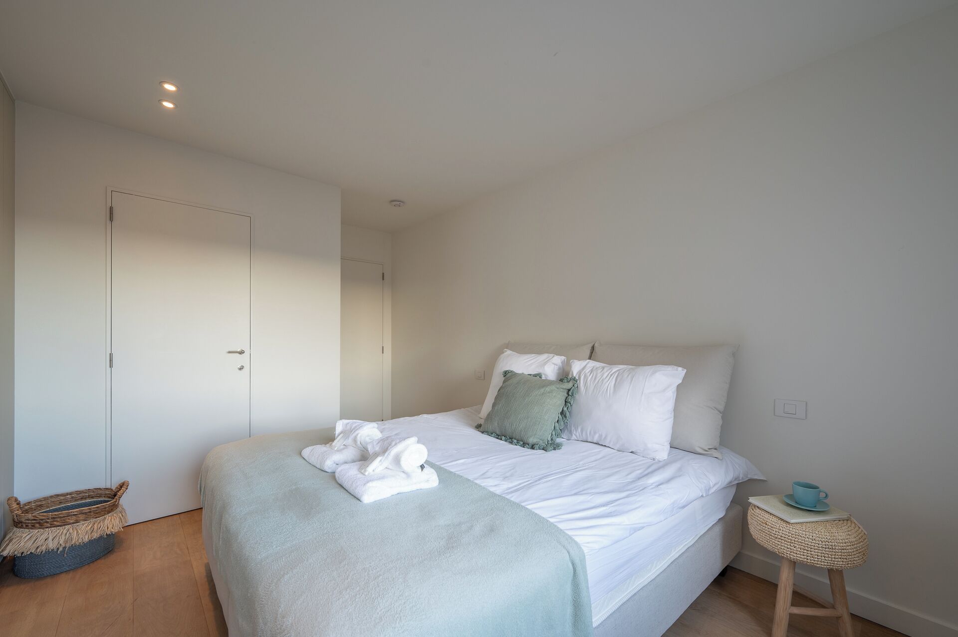 Une chambre à coucher avec un lit, des murs blancs, un plancher en bois, une petite table de chevet et un panier.