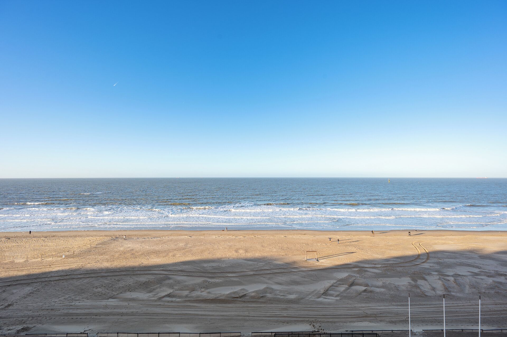 Una playa con cielo despejado, arena y algunas personas caminando.