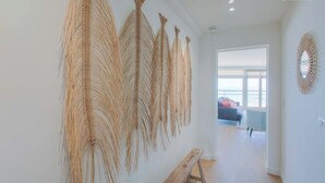 Un pasillo con un banco, un adorno en la pared y vista a una habitación con sofá y ventana.