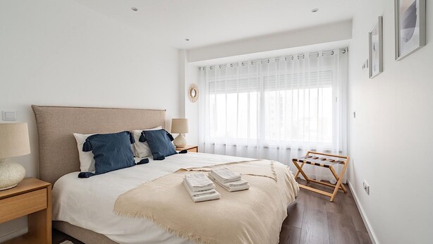 A bedroom with a large bed, bedside tables, a window with curtains, and a wooden drying rack. - Savory Beige Apartment, AC, Wifi !New! (Lisboa)