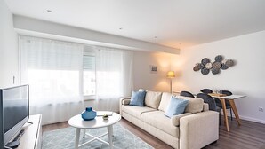 A modern living room with a sofa, a TV, a small table, and a dining area with chairs. - Savory Beige Apartment, AC, Wifi !New! (Lisboa)