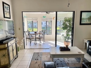 A living room with a TV, a dining table with chairs, a coffee table, and a sliding glass door leading to a patio.