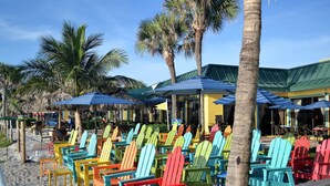 A beachside seating area with colorful Adirondack chairs and umbrellas, surrounded by palm trees. - Ready to Rest and Relax at Vero Villa- Your Vacation Home Awaits. (Vero Beach)