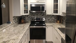 A kitchen with white cabinets, a stainless steel microwave, an oven, and a refrigerator. - Ready to Rest and Relax at Vero Villa- Your Vacation Home Awaits. (Vero Beach)