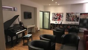 Ett vardagsrum med ett piano, svarta läderfåtöljer, en tv och abstrakt konst på väggarna.