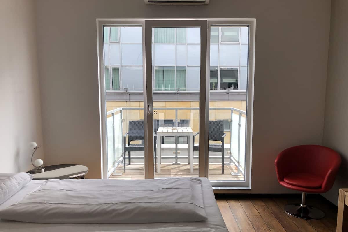 Une chambre d’hôtel avec un lit, un fauteuil rouge et un balcon équipé d’une table et de chaises.