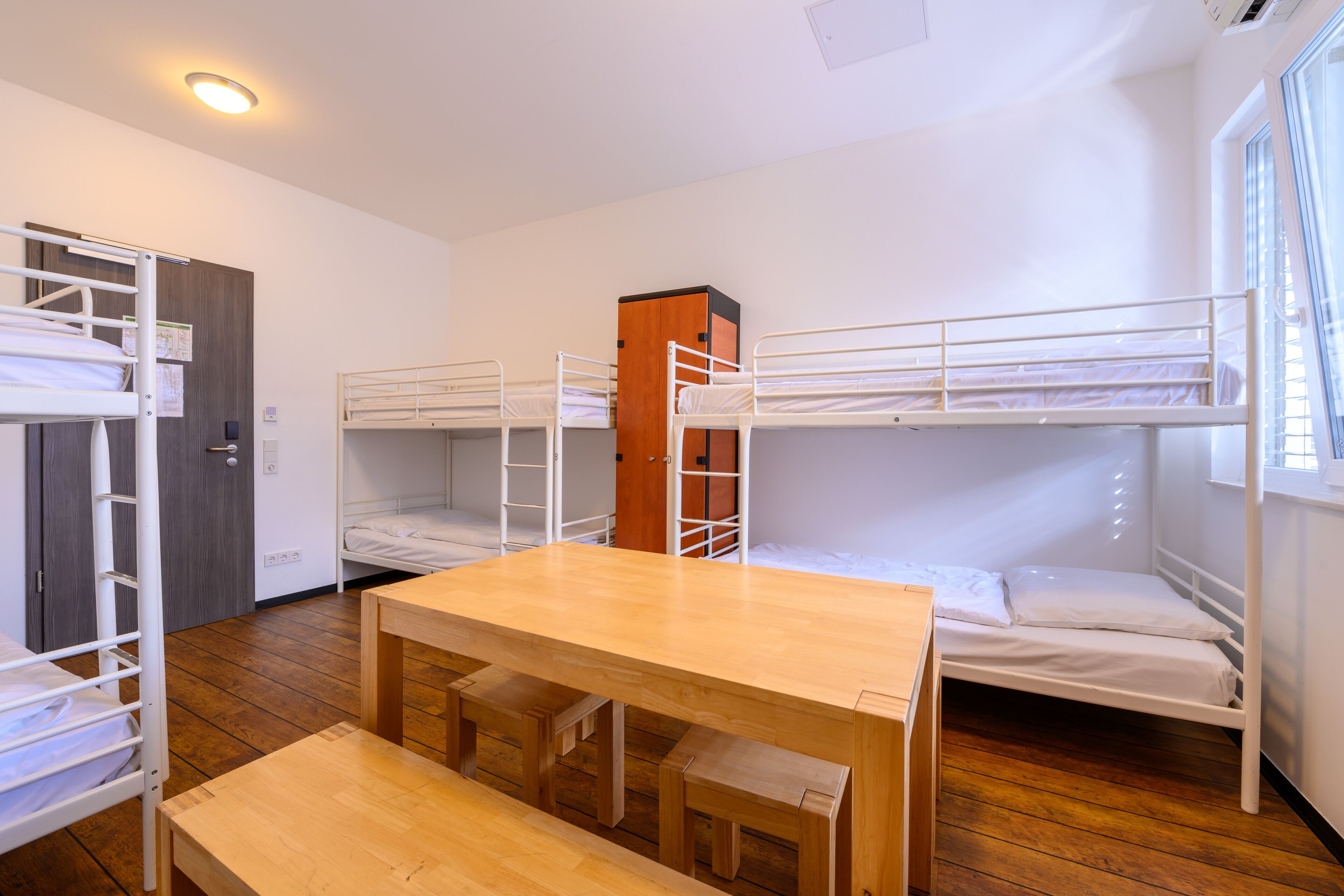 Une chambre de dortoir avec des lits superposés, une table en bois et une fenêtre.