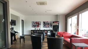Ett modernt loungeområde med ett piano, svarta och röda sittmöbler och konstverk på väggarna.