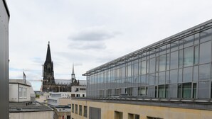 En takterrass med ett bord och en stol, med utsikt över en stadsbild med moderna byggnader och ett historiskt kyrktorn.