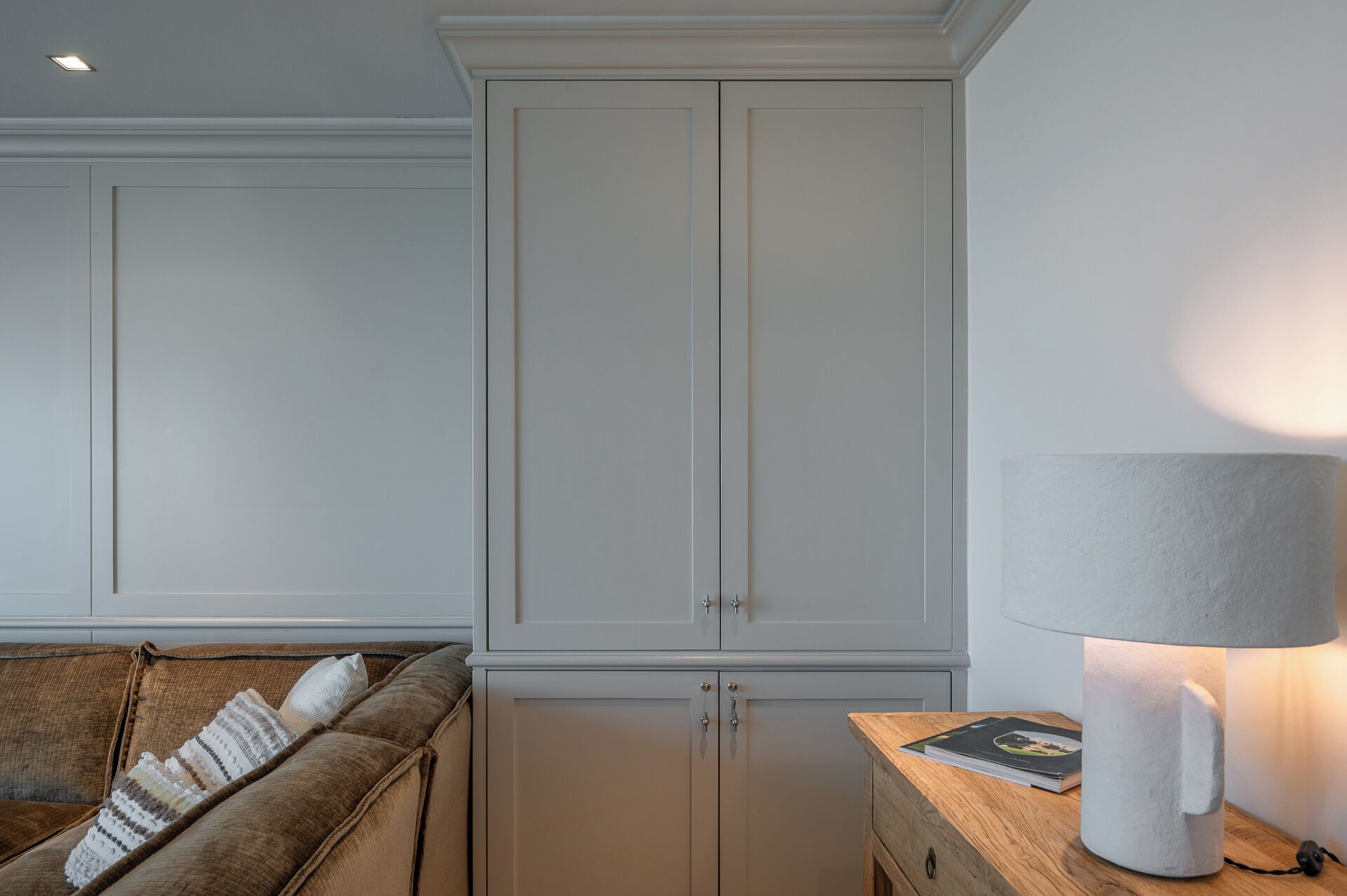 Ein Zimmer mit integriertem Kleiderschrank, einem Holznachttisch mit Lampe und einem braunen Sofa mit Kissen.