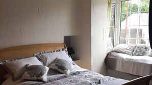 Une chambre avec un lit en bois, une table de chevet, une fenêtre avec des rideaux et une vue sur l’extérieur.