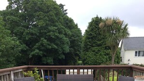 Une terrasse en bois avec des meubles en osier, notamment un canapé et deux fauteuils, ainsi qu’une petite table.