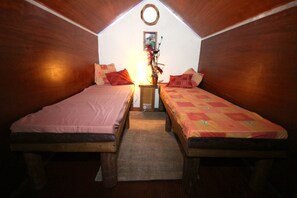 A small, cozy room with two wooden beds, a small table with a lamp, and a wall-mounted picture. - Secluded Meadow, Unique Shire Hut, Perfect Camping (Camborne)