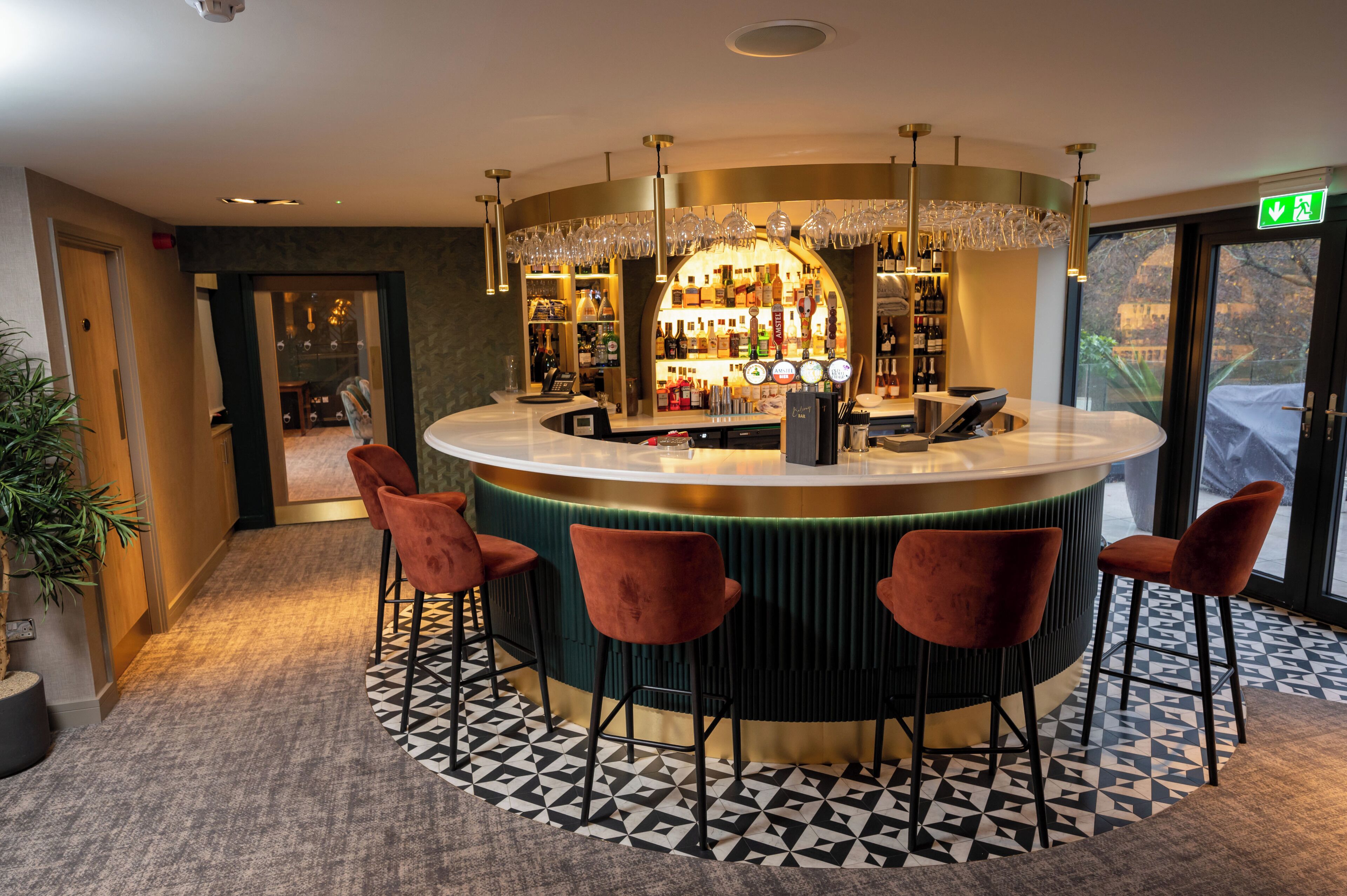 A bar area with a circular bar, multiple stools, and a variety of bottles and glasses on shelves.