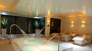 Un área de piscina interior moderna con techo de vidrio, asientos a la orilla de la piscina e iluminación ambiental.
