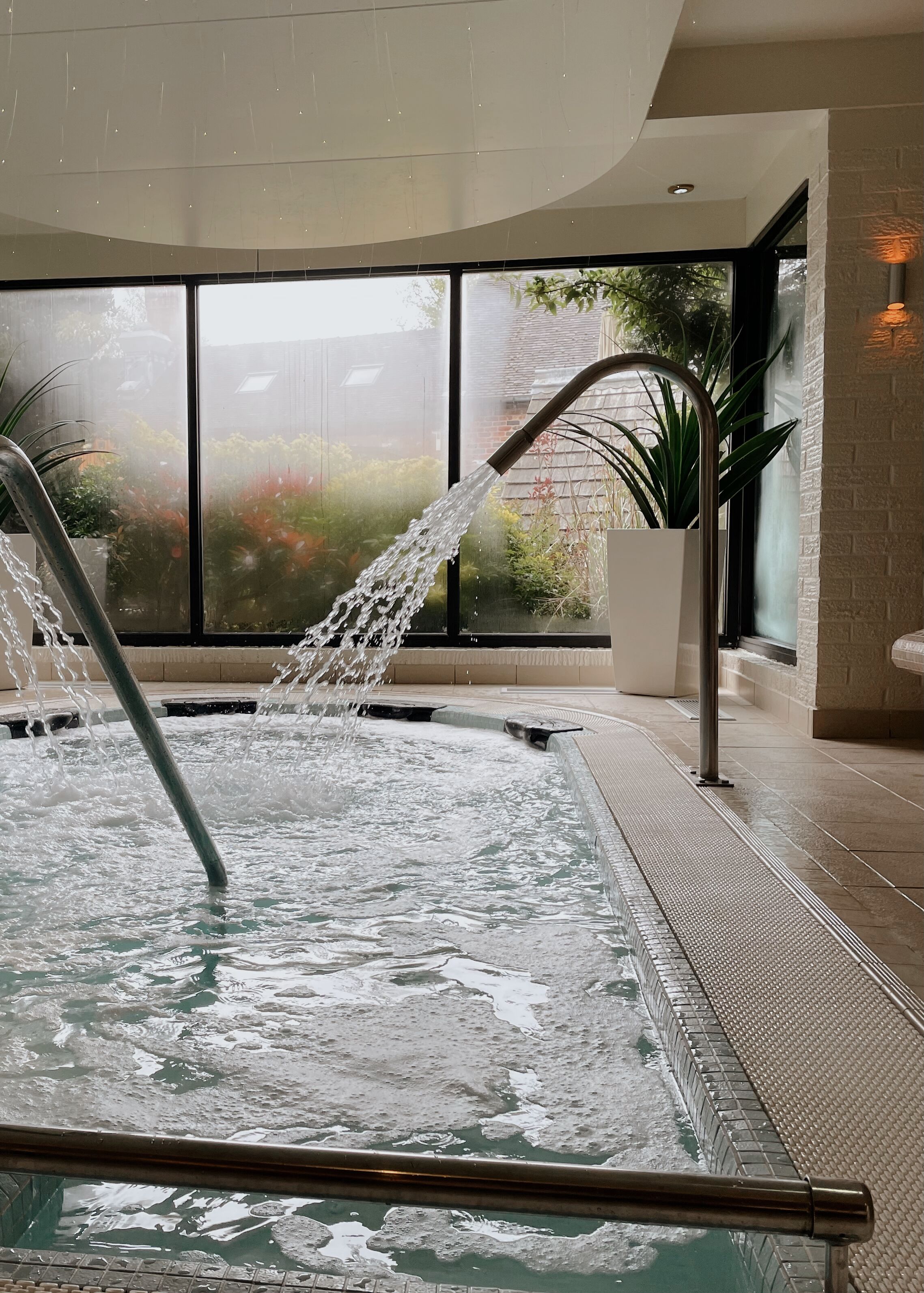A spa area with a hot tub, a water feature, and a large window with a view of greenery.