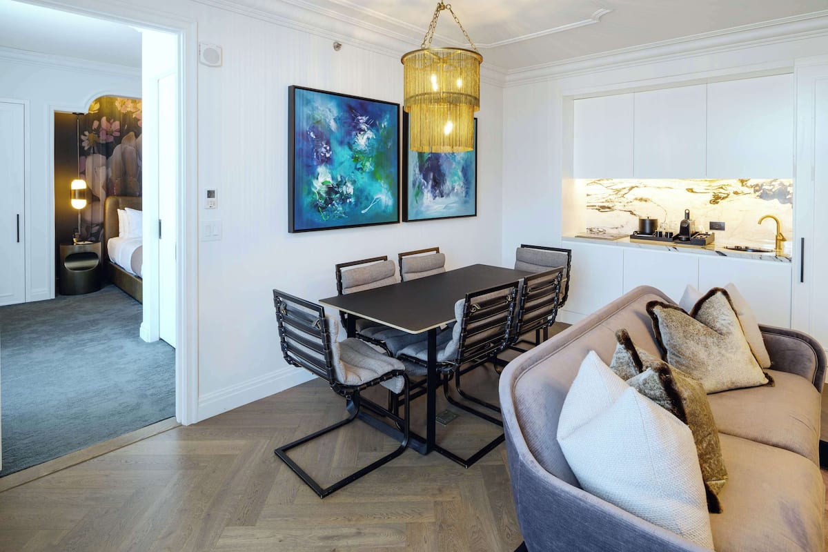 Ett modernt hotellrum med en matplats som har ett mörkt träbord och stolar, en kristallkrona och två abstrakta målningar.
