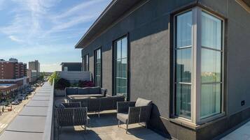 Un edificio moderno con grandes ventanales y una terraza en la azotea con mobiliario de exterior.