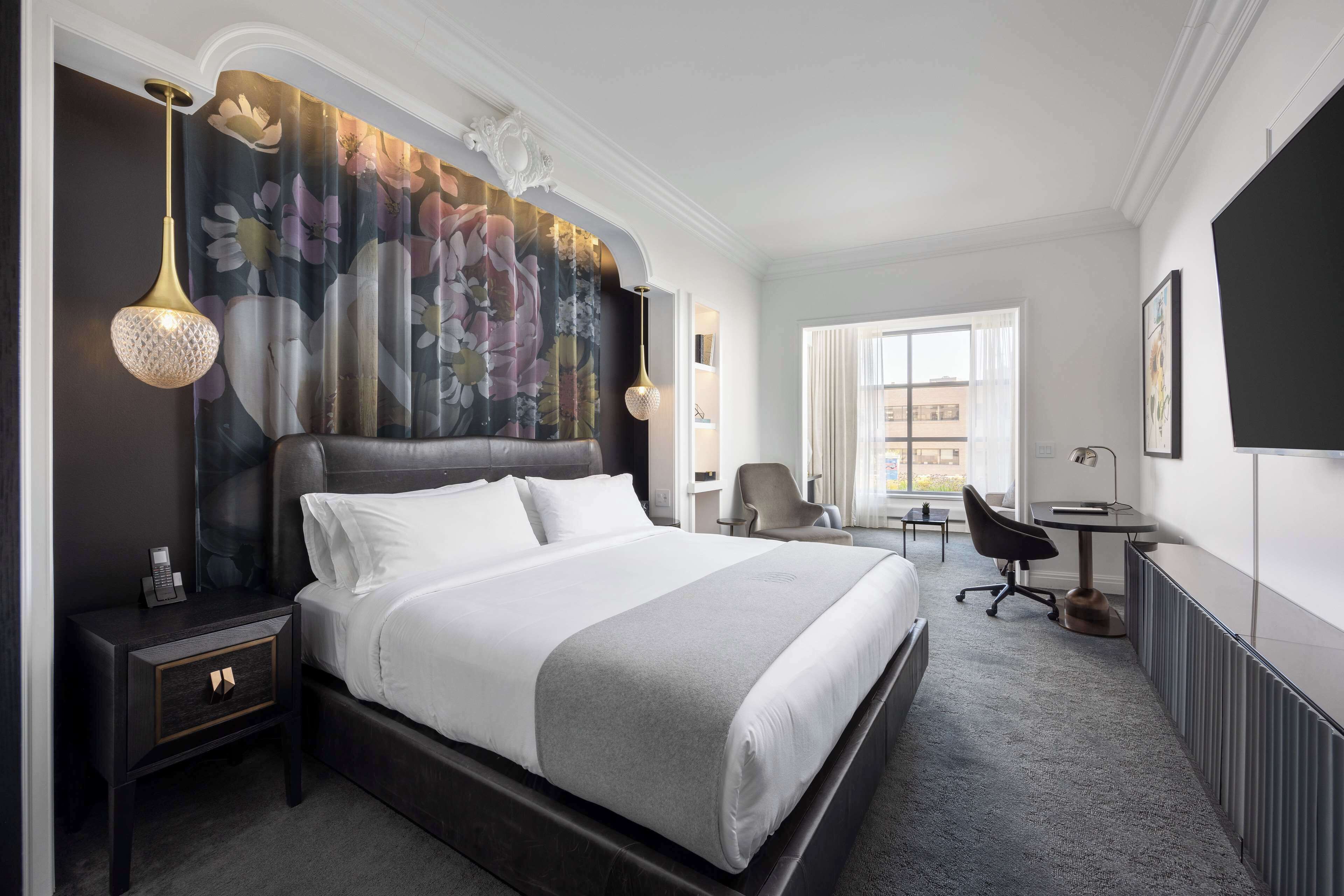A modern hotel room with a large bed, a nightstand, a desk, and a chair.