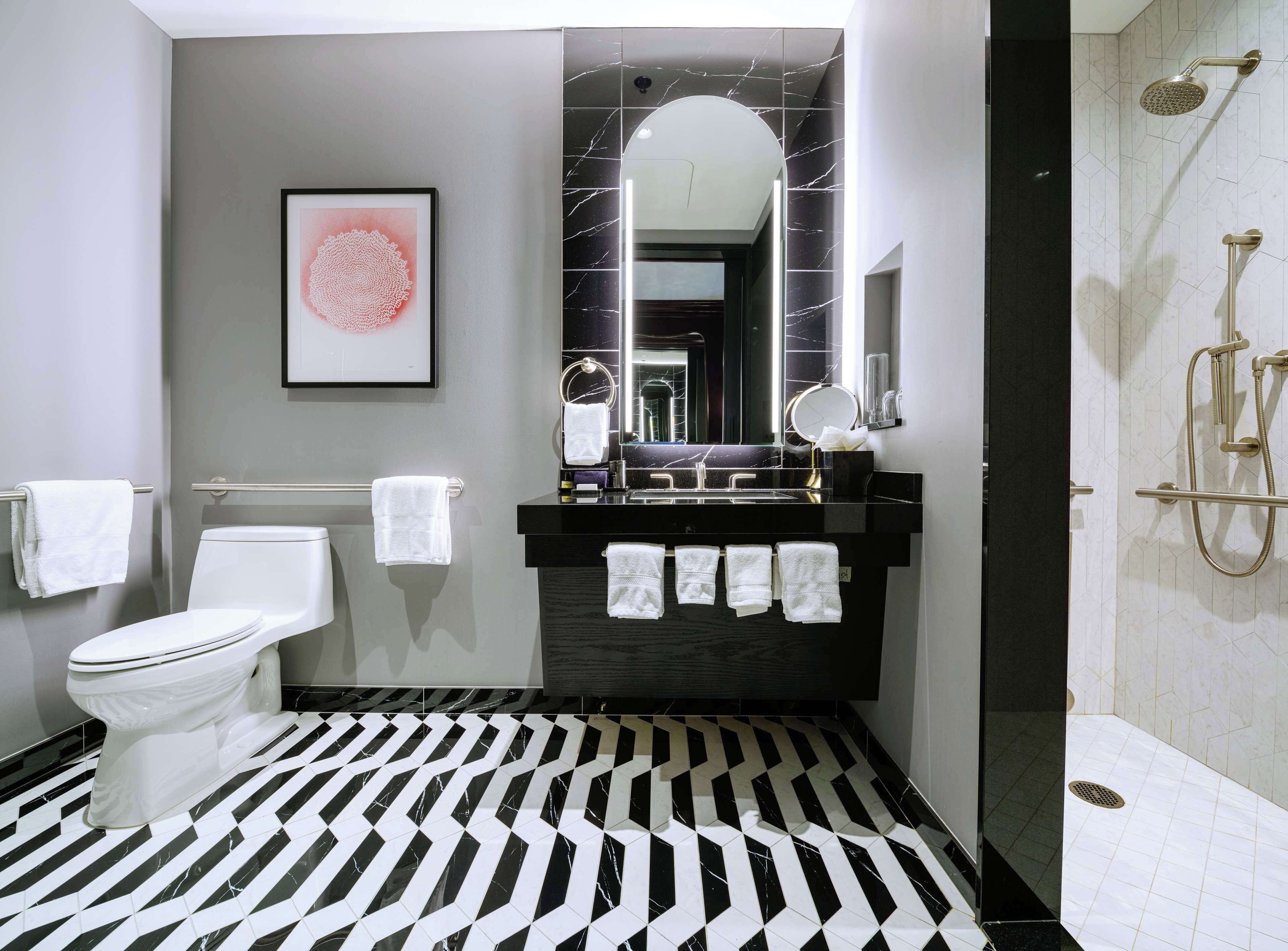 A modern bathroom with a black and white patterned floor, a toilet, a sink with a mirror, and a shower area.