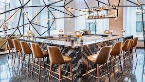 Zona de bar moderna con encimera de mármol, varios taburetes y diseño geométrico en el techo.