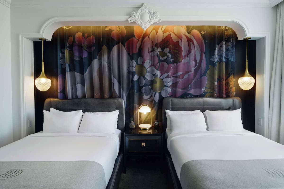 Ett hotellrum med två sängar, en stor väggmålning med blommotiv och en modern kristallkrona.