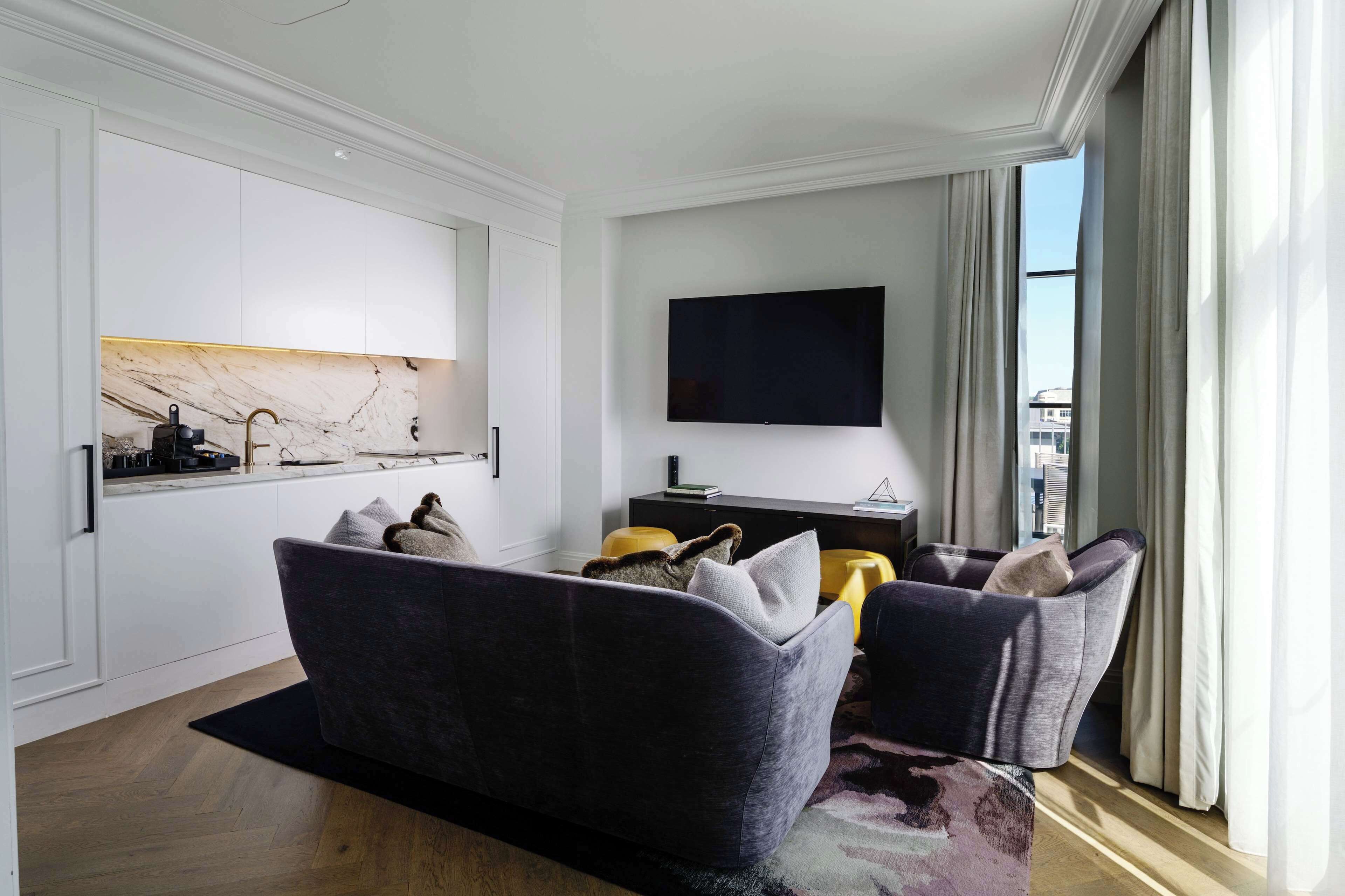 A modern living room with a sofa, a flat-screen TV, and a marble backsplash.